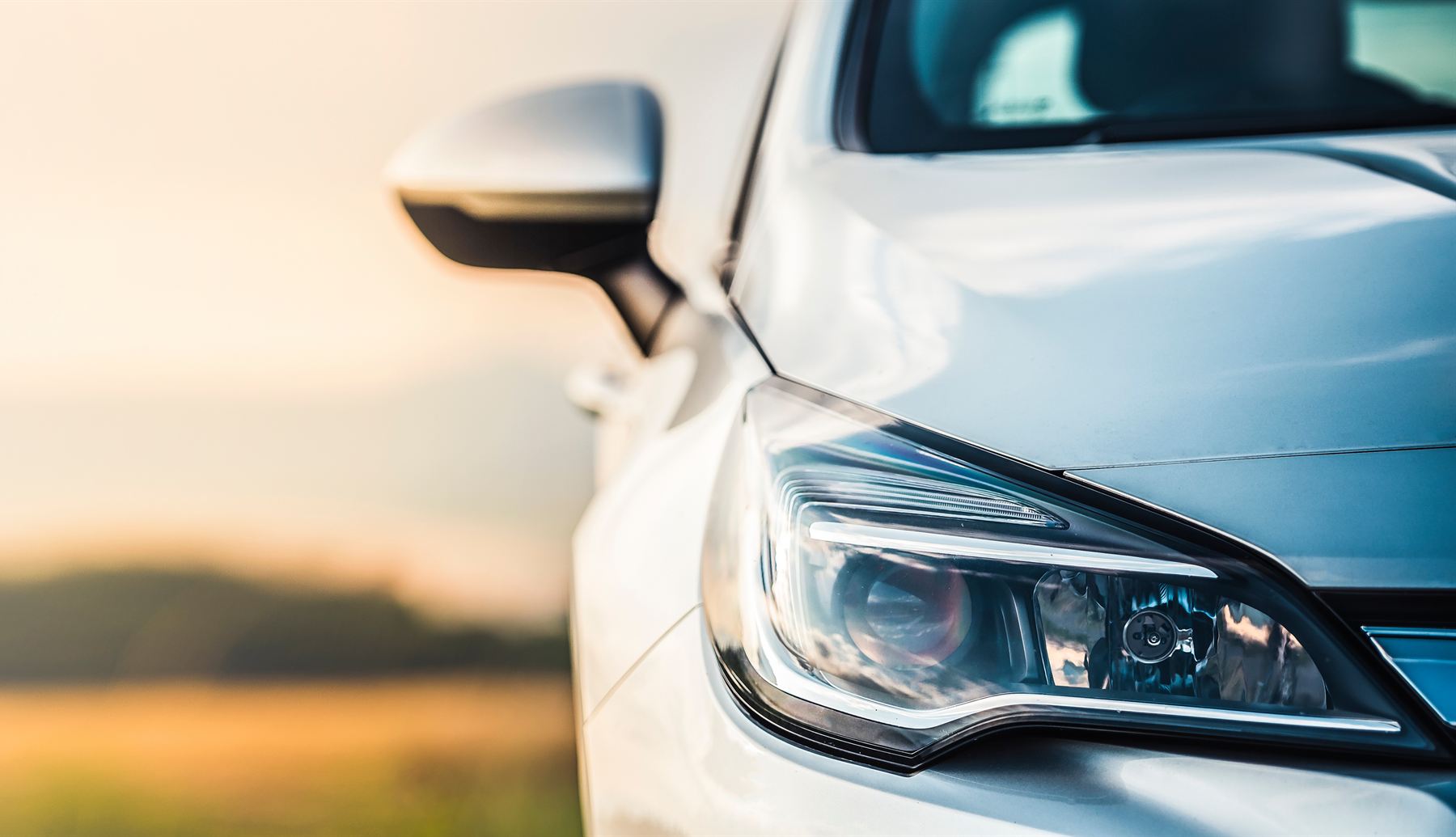 Front of a silver car parked in open country at sunset